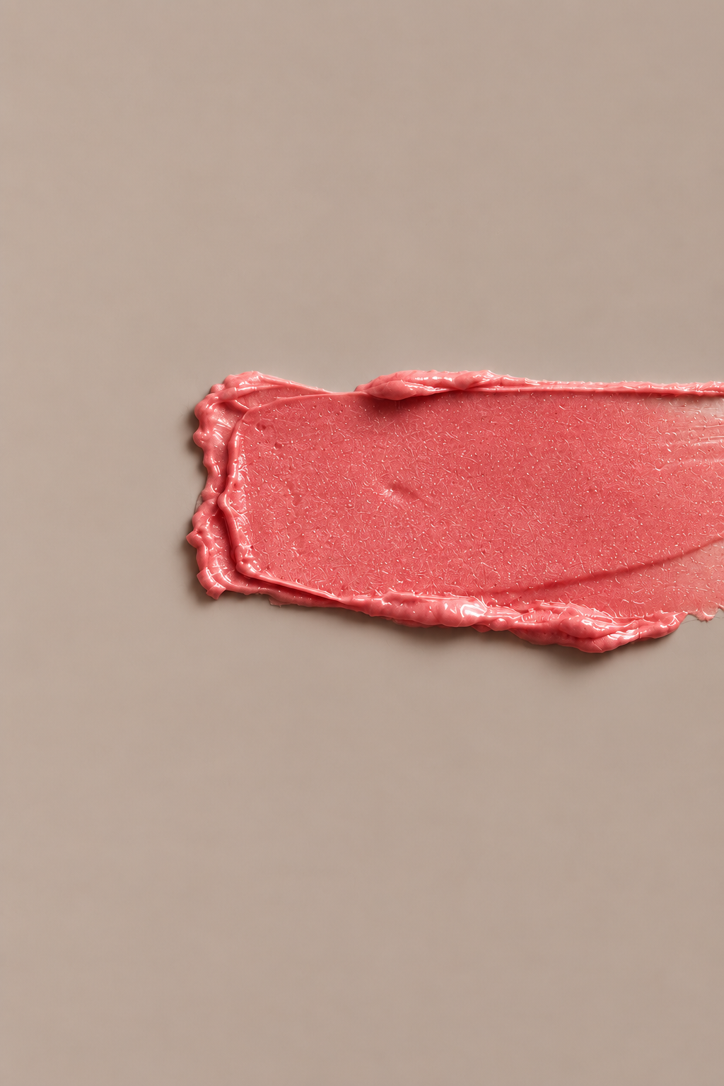 A textured swipe of shimmering pink blam on a solid taupe background.
