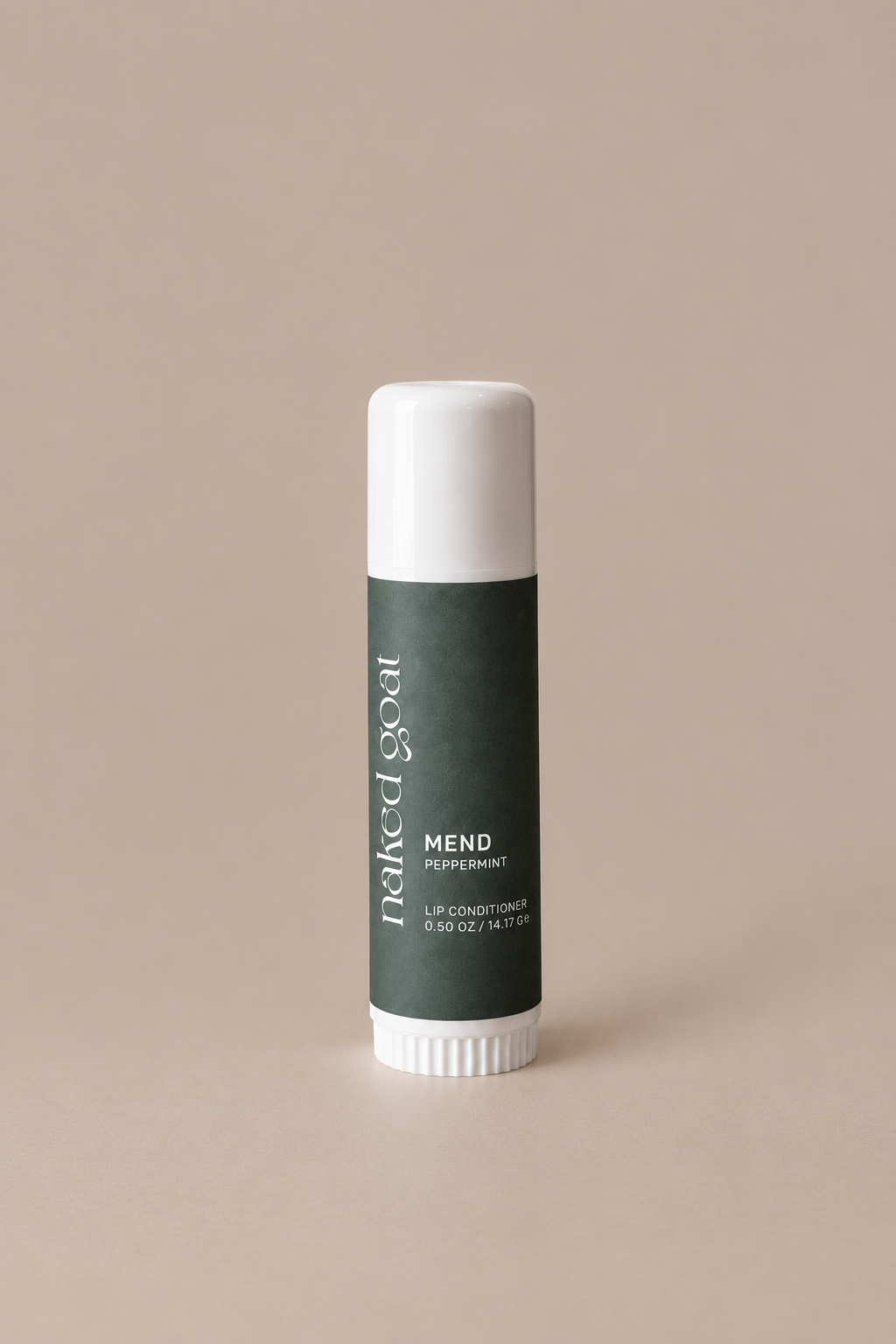 A single lip balm tube standing upright on a plain warm beige background. The tube has a white cap and base with a dark green label reading 'naked goat' and 'MEND PEPPERMINT'.