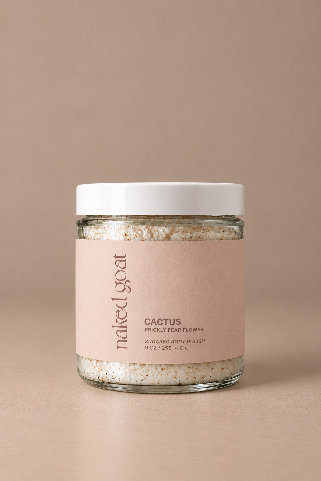 A glass jar of Naked Goat Cactus Sugared Body Polish with a white lid and a light pink label, set against a solid beige background.