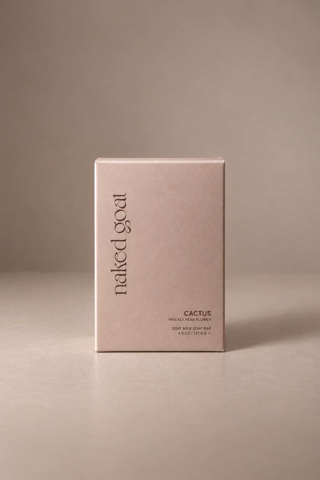 A minimalist, light blush pink rectangular soap box for 'naked goat' Cactus scent, standing upright on a matching neutral beige surface against a solid taupe background.