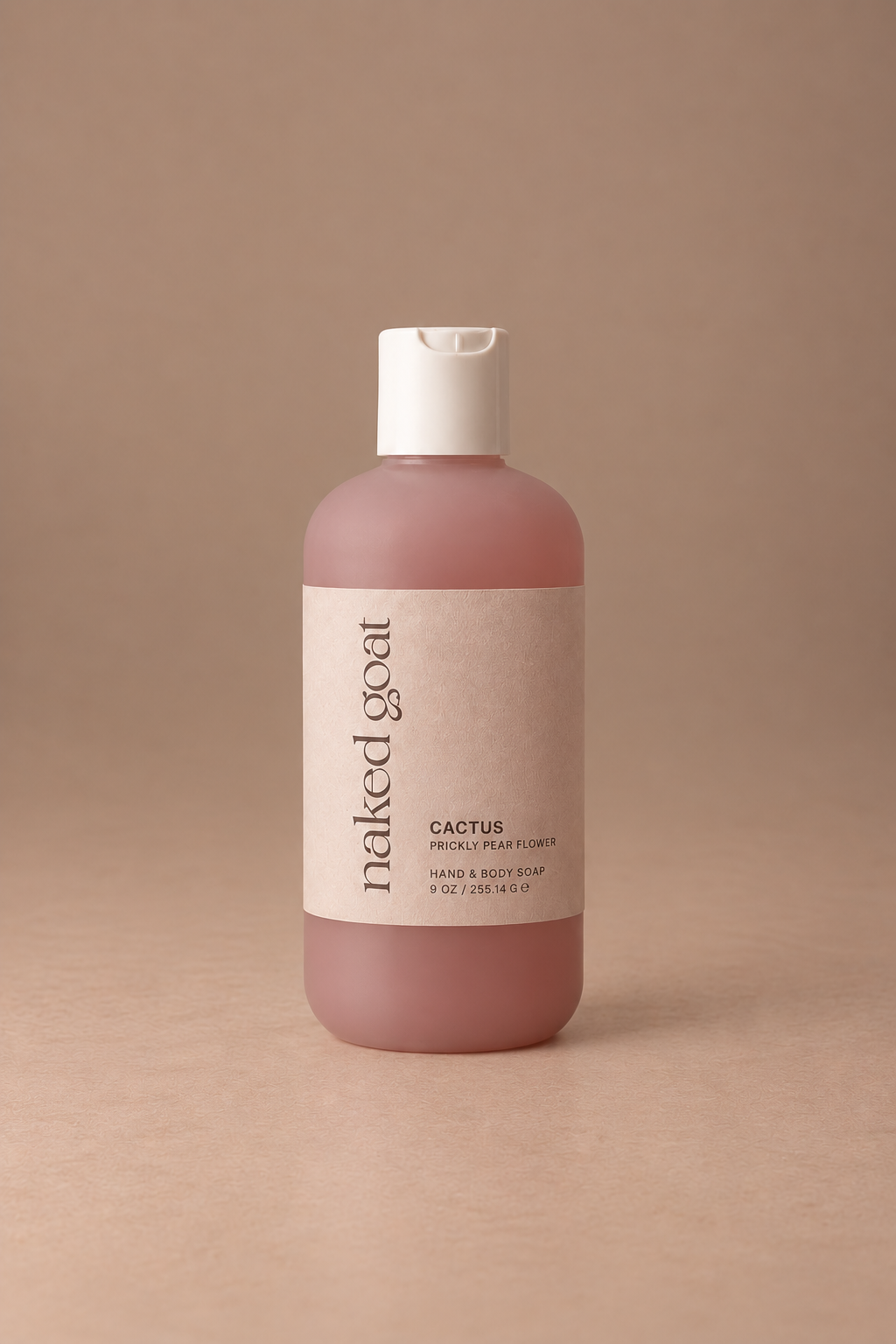 A bottle of Naked Goat Cactus Hand & Body Wash with a dusty pink translucent body, a white flip-top cap, and a beige label, set against a solid warm beige background.