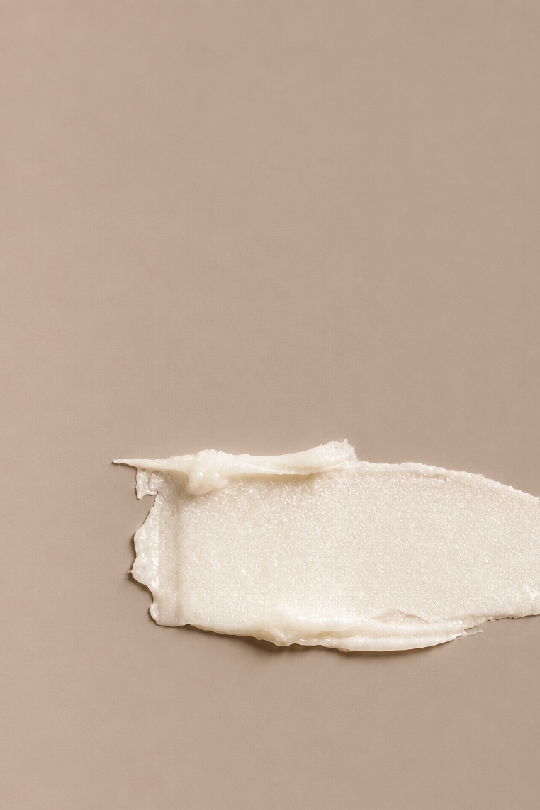 Luxe lip conditioner creamy balm texture swatch on a seamless mushroom studio background.