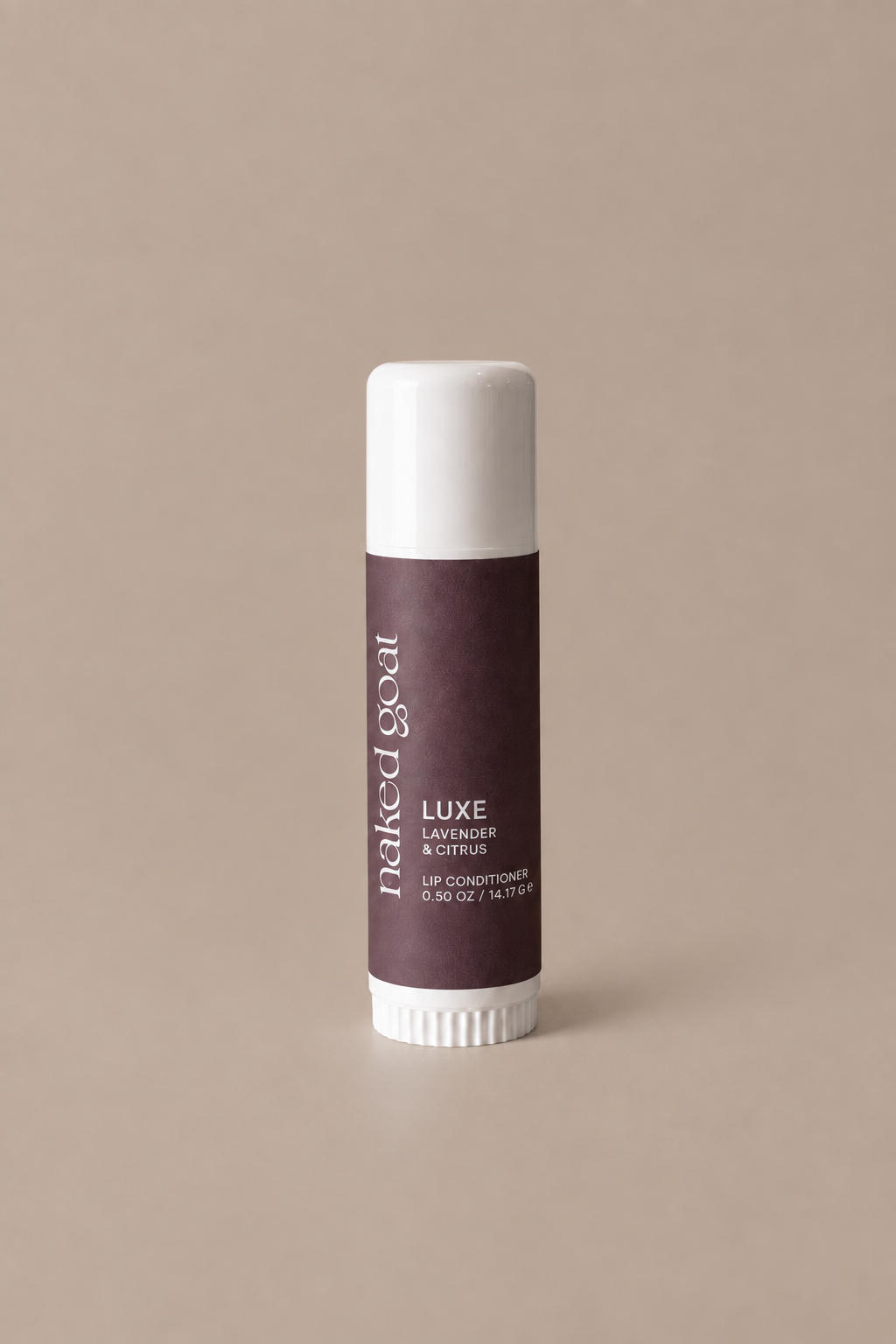 A single lip balm tube standing upright on a plain warm beige background. The tube has a dark plum-brown label with white text reading 'Naked Goat' and 'LUXE', plus smaller text Lavender & Citrus.