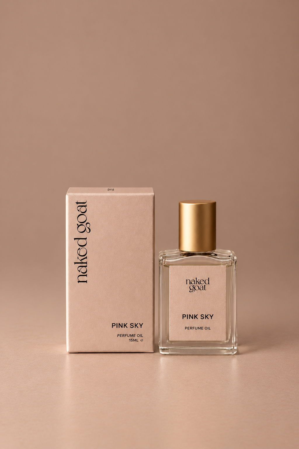 A bottle of Naked Goat Pink Sky perfume oil stands next to its matching pink packaging box on a warm beige surface against a matching beige background.
