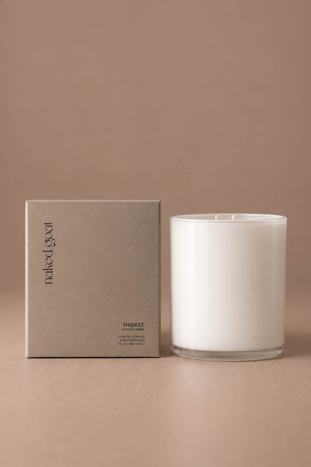 Naked Goat Thicket sage and amber pure soy candle in a white glass vessel with matching box on a seamless mushroom studio background.